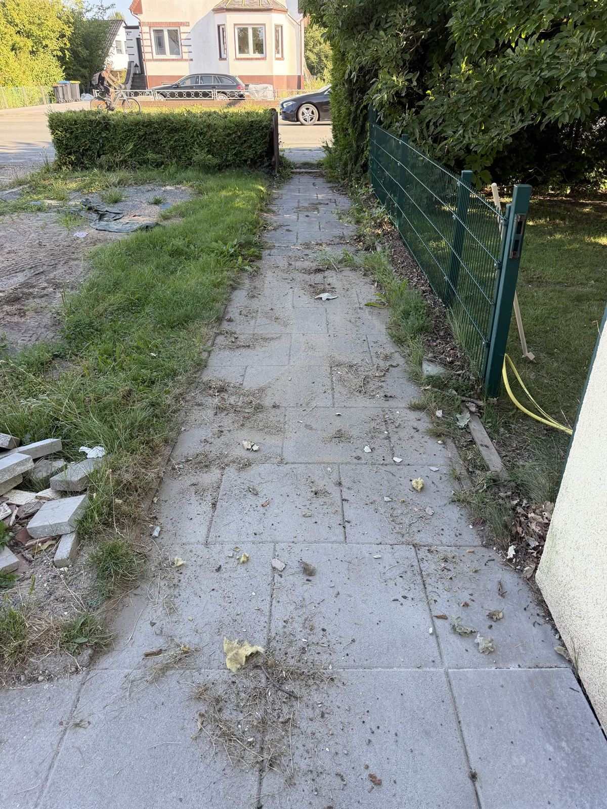 Plattenweg neben einem Haus vor der Reinigung, bedeckt mit Laub, Erde und Grasresten