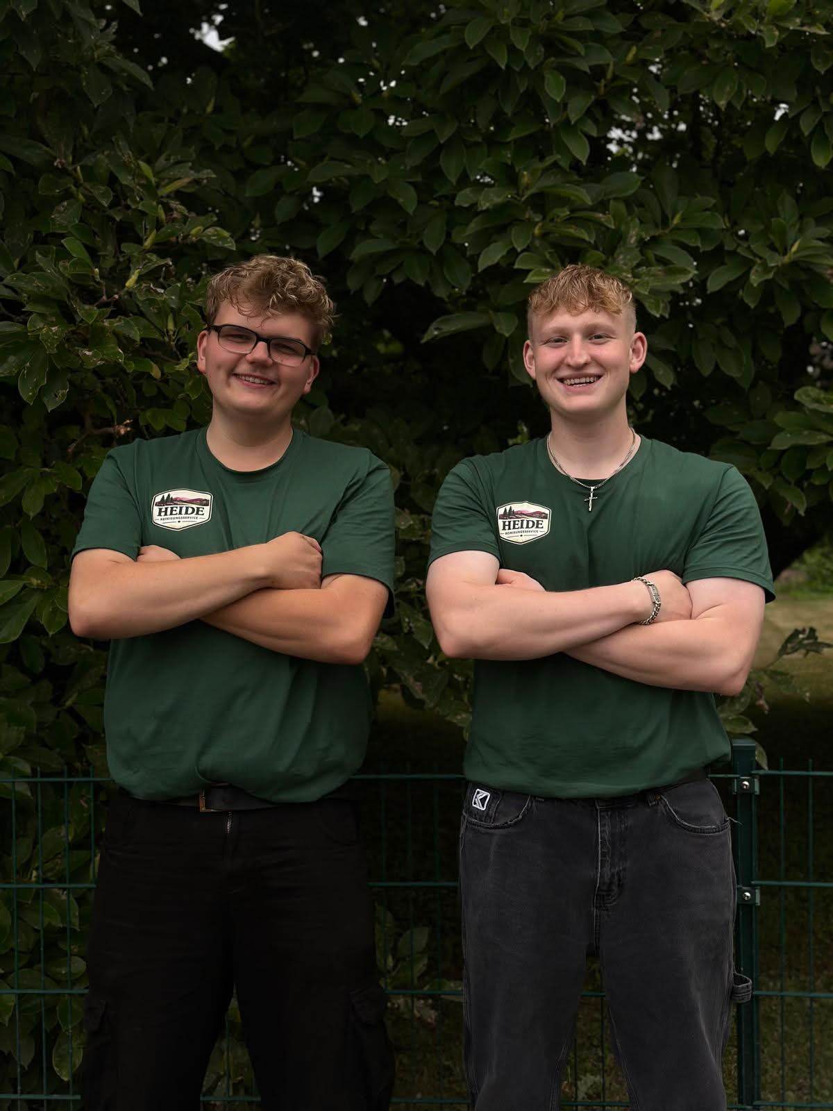 Mads und Pierre von Heide Reinigungsservice in grünen Firmen-Shirts vor einer Hecke